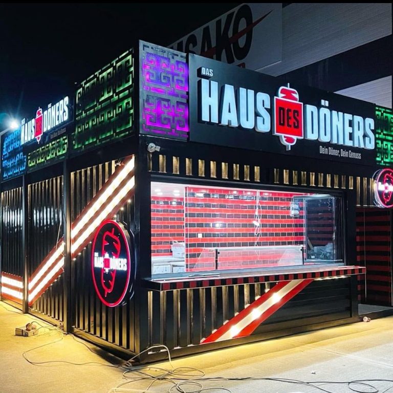 Haus des Döners – LED-Foodcontainer mit Verkaufsfenster Gastronomiecontainer mit LED-Fassade bei Nacht – Haus des Döners mit Glas-Front, rotem Fliesendesign und Verkaufsmodul